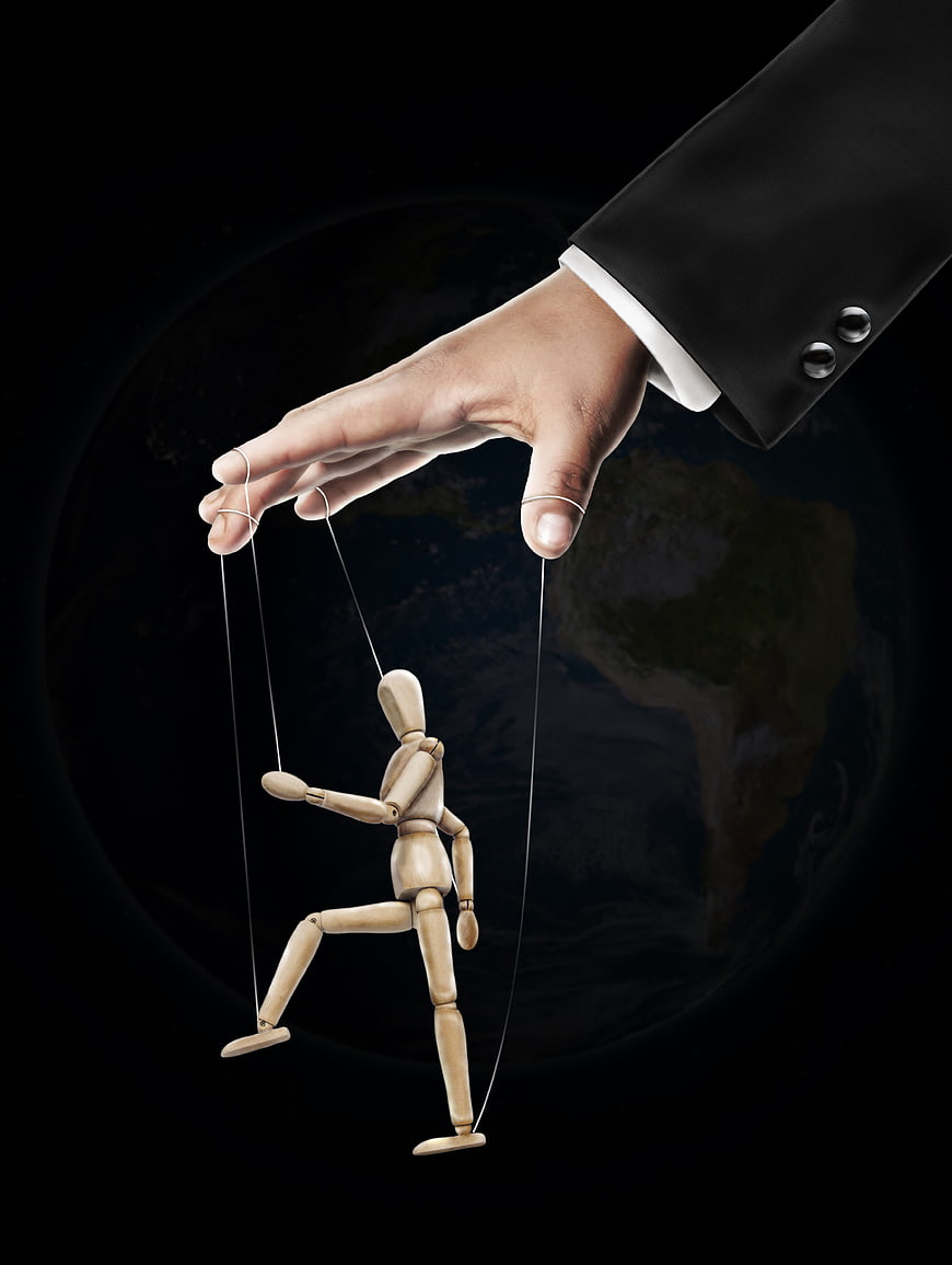 Business hand controlling wooden puppet with globe background