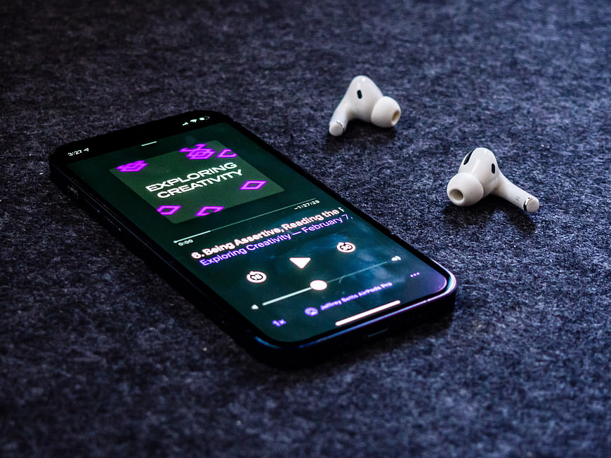 Smartphone Playing Podcast with Wireless Earbuds on Dark Surface