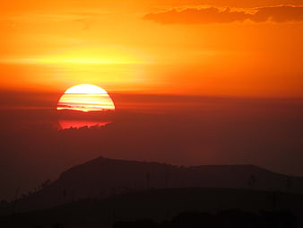 Vibrant orange sunset over silhouetted hills and clouds