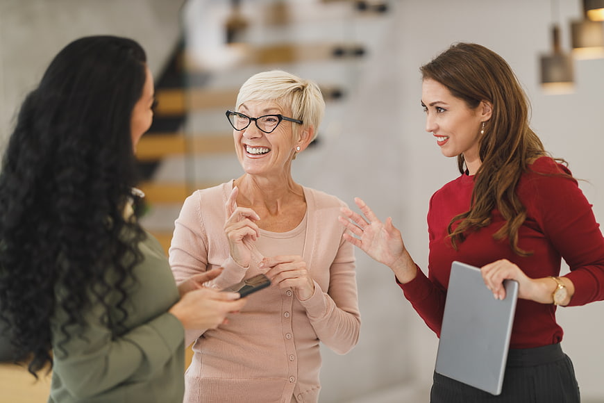 Three diverse women laughing and talking in modern office
