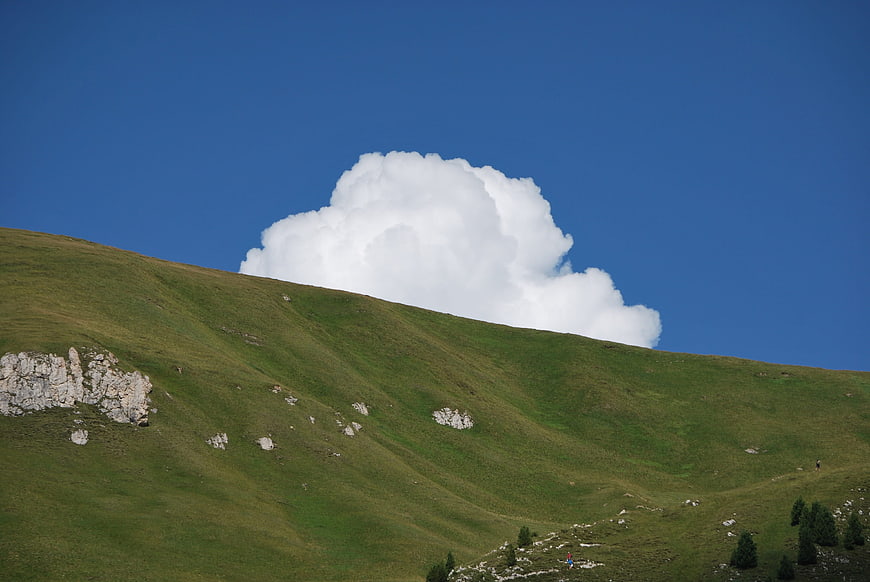 Green Mountain Slope with Large White Cloud Against Blue Sky