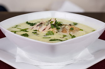 Creamy chicken soup with herbs in white bowl