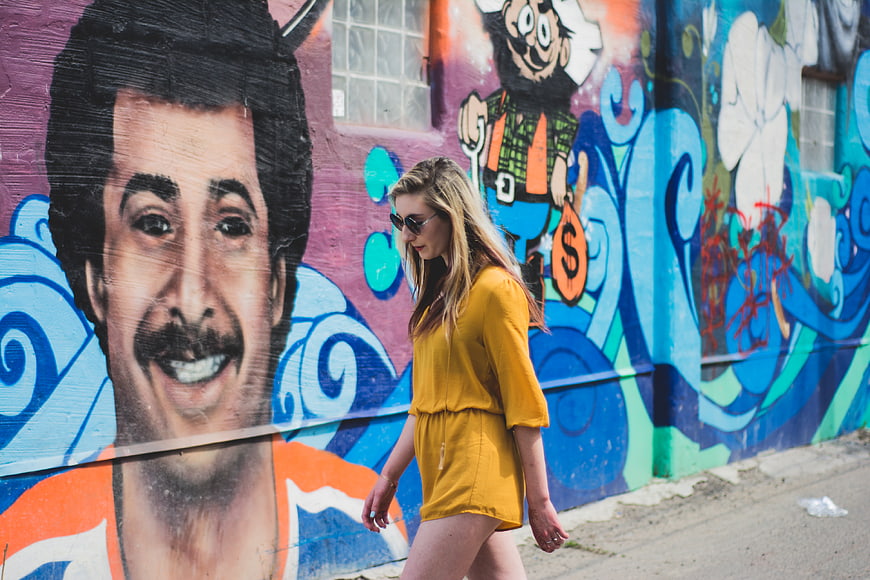 Woman in Yellow Dress Walking Past Colorful Graffiti Mural