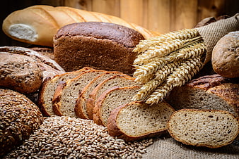 Assortment of artisan breads, wheat stalks, and grains on rustic wood