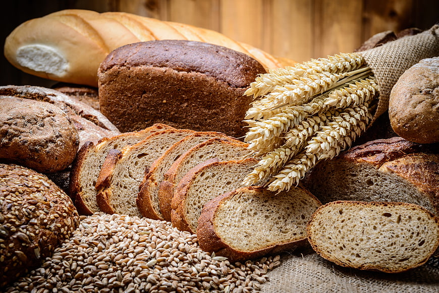 Assortment of artisan breads, wheat stalks, and grains on rustic wood