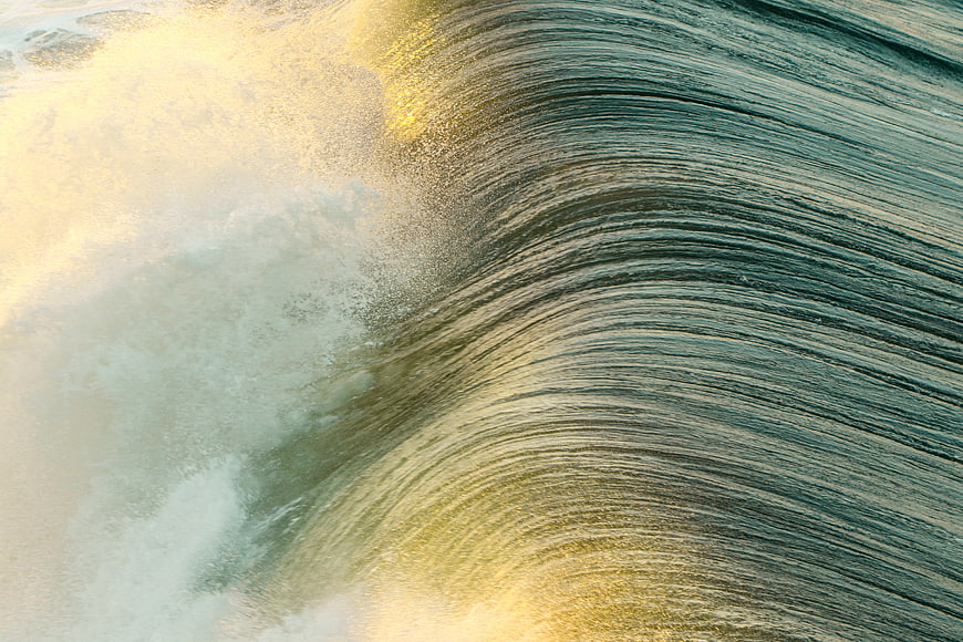 Close-up of a curling ocean wave with golden sunlight