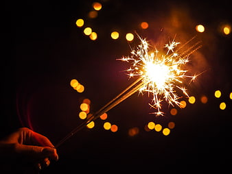 Hand holding sparkler with bokeh lights at night