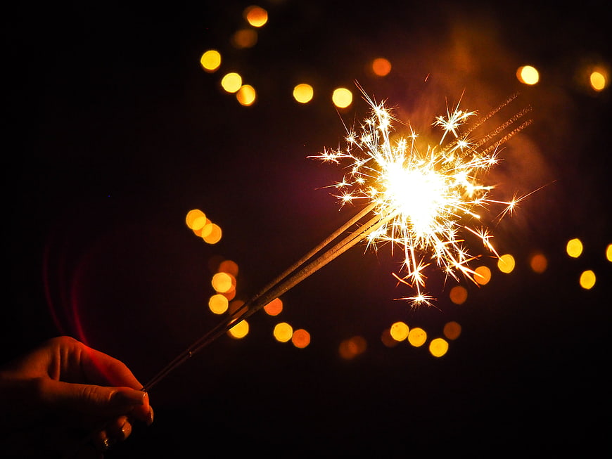 Hand holding sparkler with bokeh lights at night