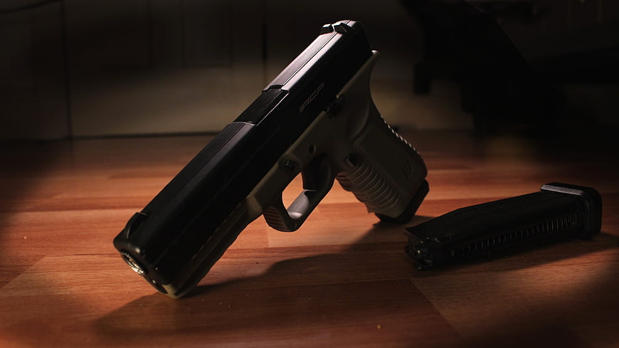 Black handgun and magazine on wooden floor