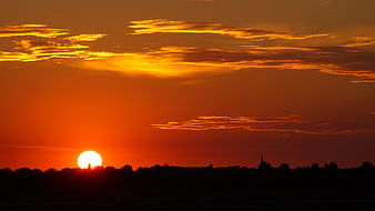 Vibrant Orange Sunset Over Silhouetted Landscape
