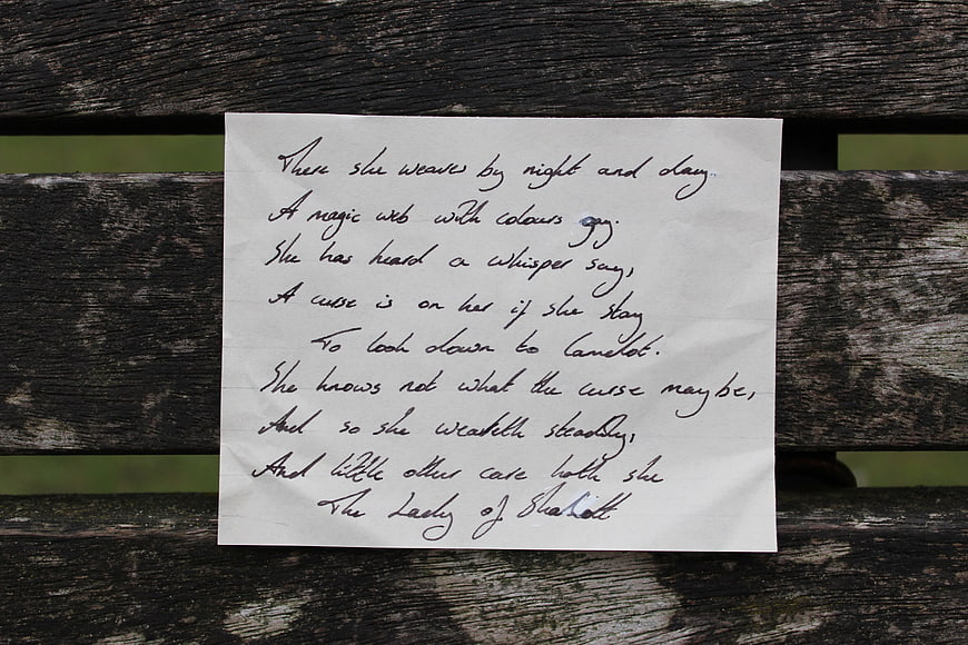 Handwritten Poem on White Paper Resting on Weathered Wooden Bench