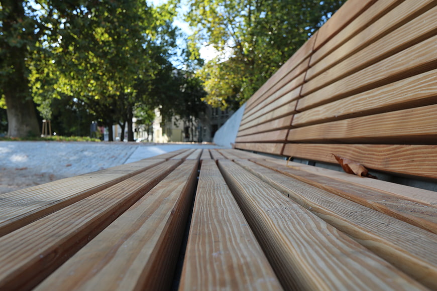 Close-up of wooden park bench slats with blurred green trees