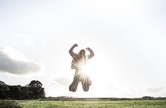 Silhouette of person jumping in field with sunburst