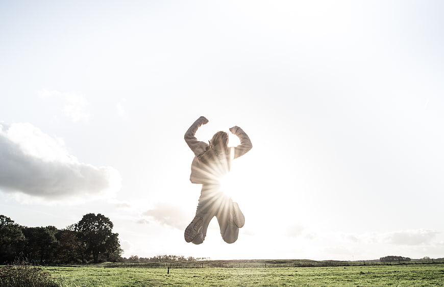 Silhouette of person jumping in field with sunburst