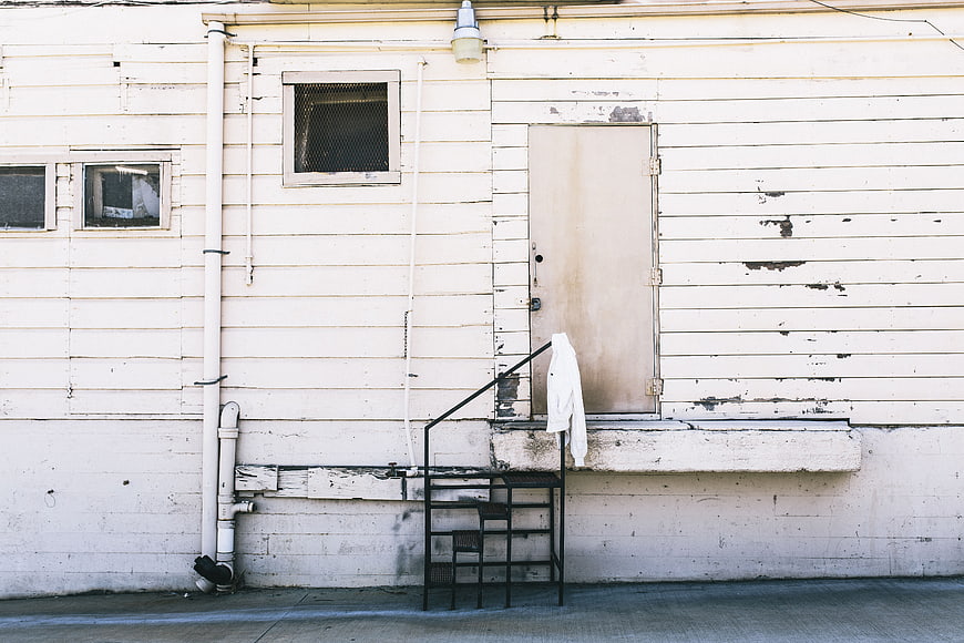 Weathered white building exterior with metal stairs and hanging jacket