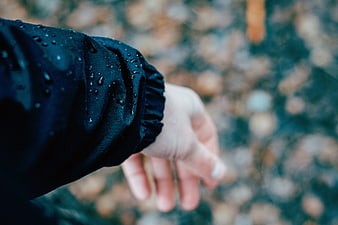 Close-up of hand in wet black jacket sleeve with raindrops