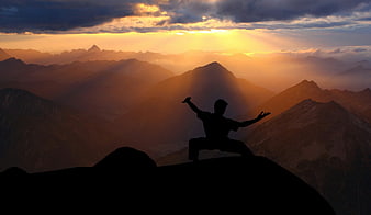 Silhouette of martial artist performing tai chi on mountain peak at sunset