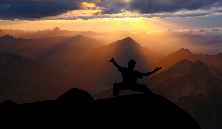 Silhouette of martial artist performing tai chi on mountain peak at sunset