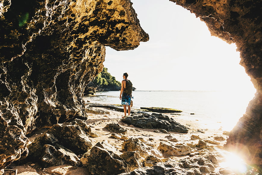 Man standing in a rocky sea cave looking out at the ocean