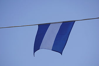 Blue and White Striped Flag Hanging on Wire Against Sky