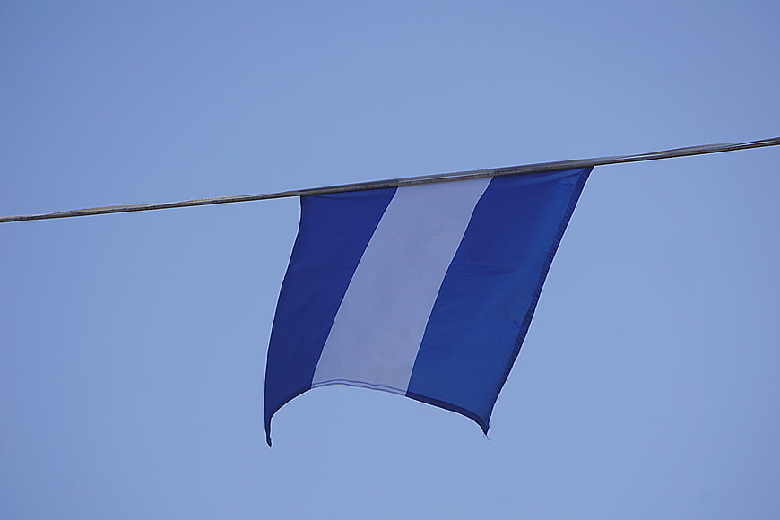 Blue and White Striped Flag Hanging on Wire Against Sky
