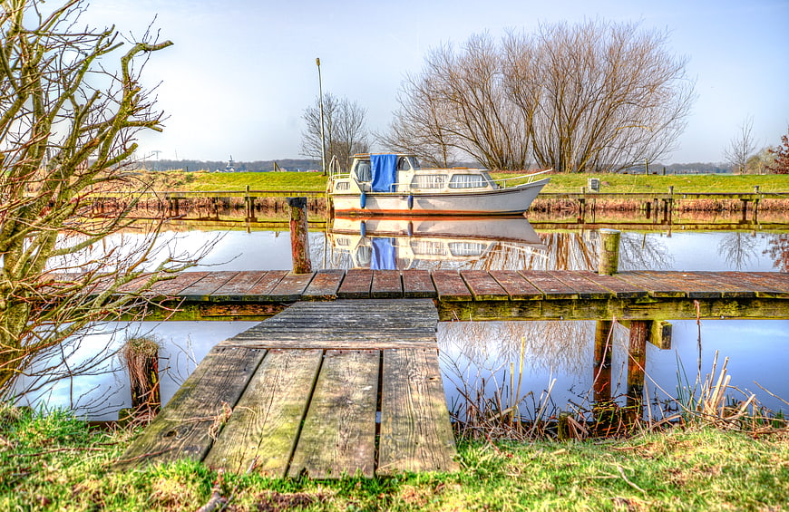 White boat docked in canal with wooden pier