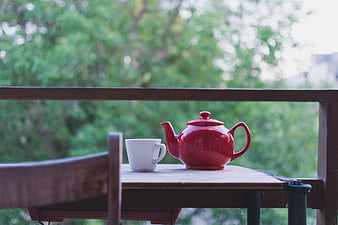 Red Teapot and White Cup on Wooden Table with Green Background