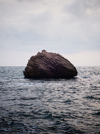 Lone Rock in Ocean Under Overcast Sky