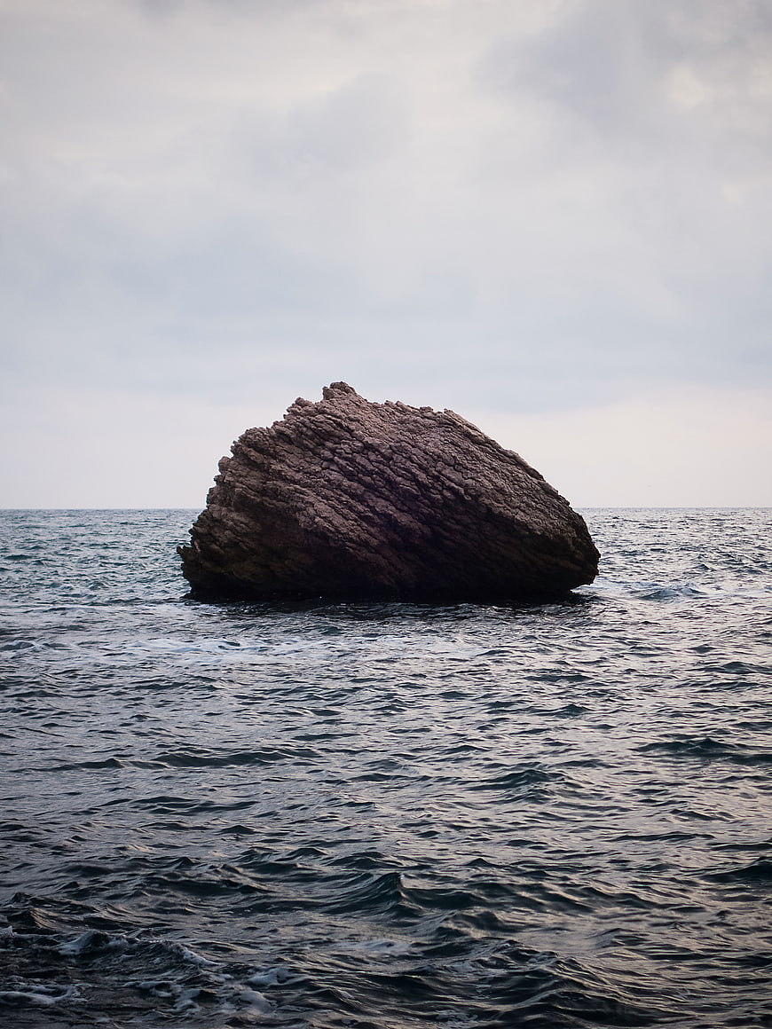 Lone Rock in Ocean Under Overcast Sky