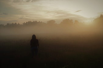 Silhouette of woman walking in foggy field at sunrise