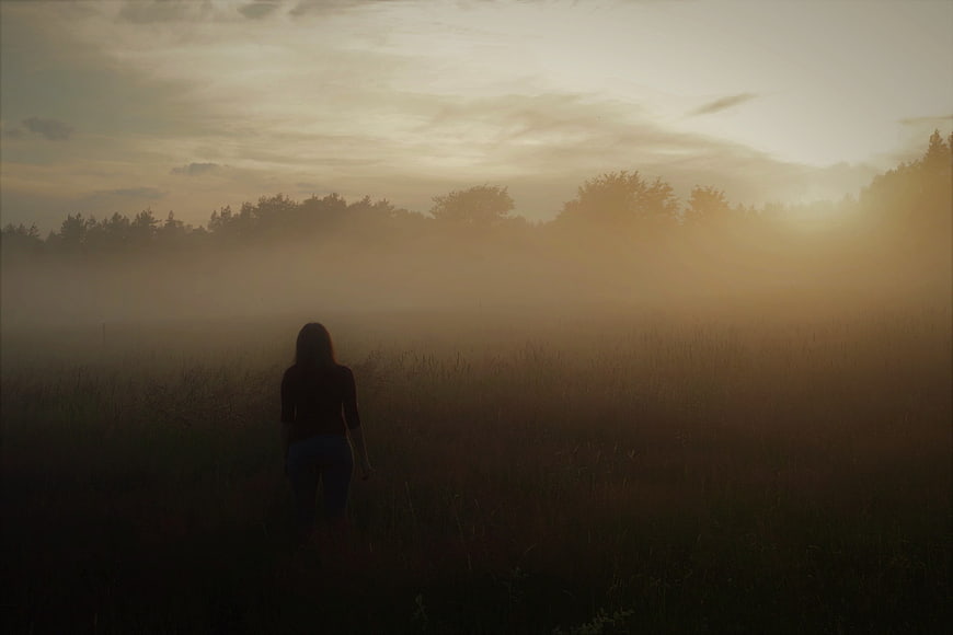 Silhouette of woman walking in foggy field at sunrise