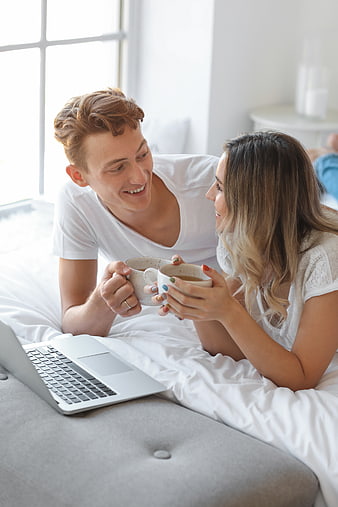 Happy young couple drinking coffee in bed with laptop
