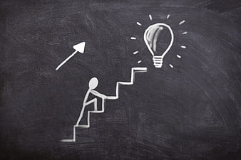 Chalk drawing of person climbing stairs toward lightbulb on blackboard