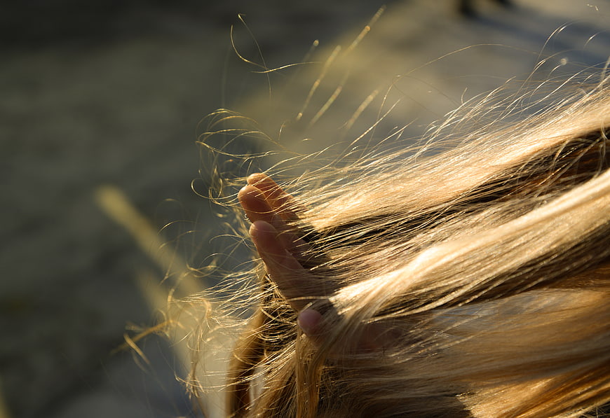 Close-up of hand running through sunlit blonde hair