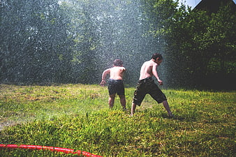 Two boys playing in sprinkler water spray on grass