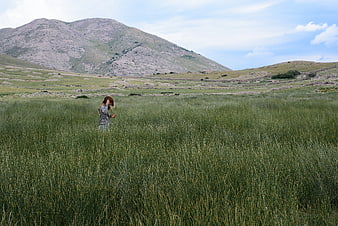 Woman walking in tall green grass with mountain landscape background