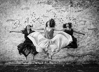 Three women jumping in front of textured wall with flying birds
