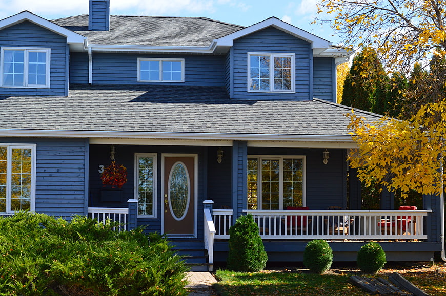 Blue two-story suburban house with front porch in autumn
