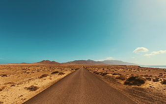 Endless Desert Road Leading to Mountains Under Blue Sky
