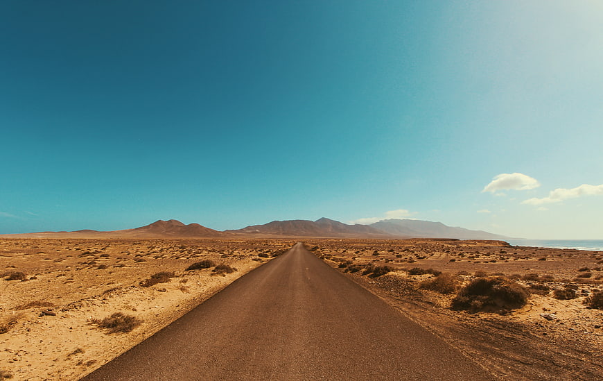 Endless Desert Road Leading to Mountains Under Blue Sky
