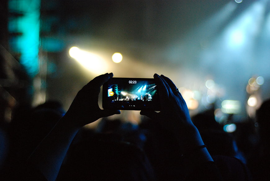 Hands recording concert on smartphone screen