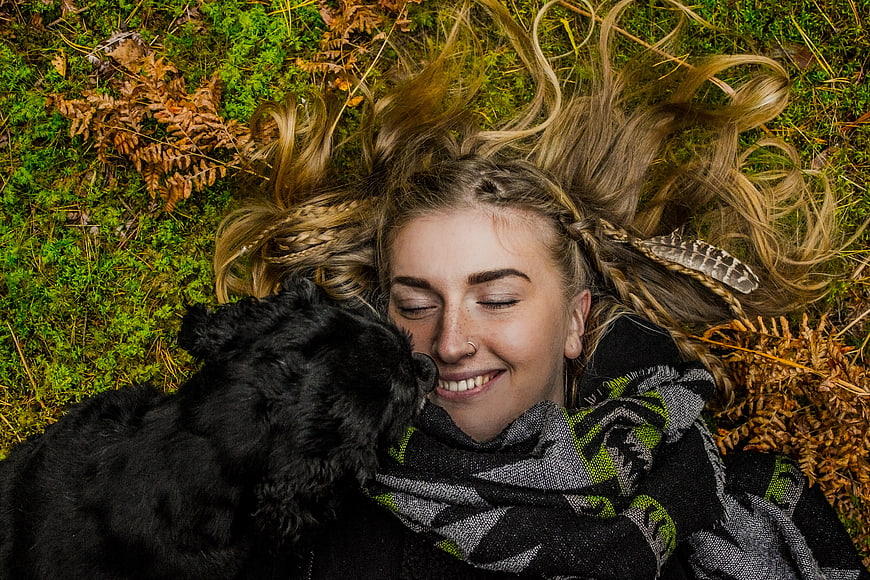 Happy woman lying in grass with black dog