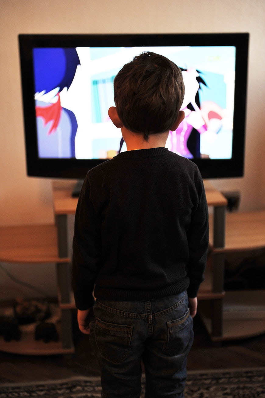 Young boy watching cartoons on television from behind