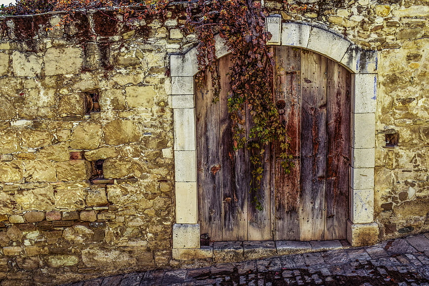 Weathered wooden door in ancient stone wall with ivy