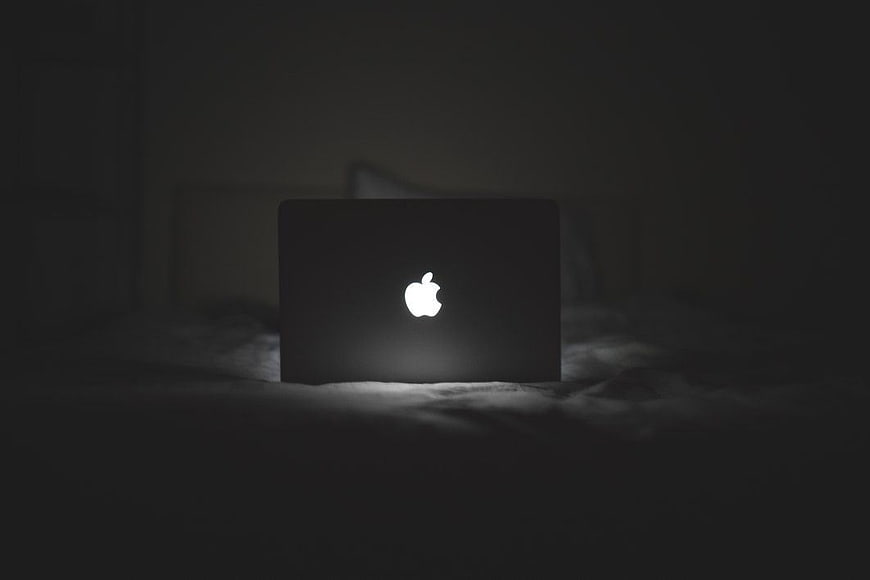 Glowing Apple Logo on MacBook in Dark Room