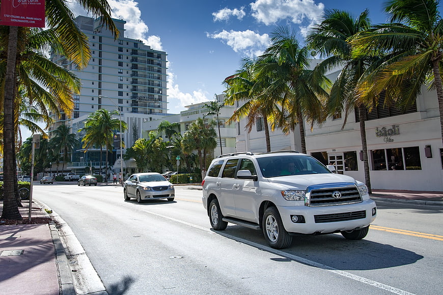 White SUV driving on sunny Miami Beach street with palm trees