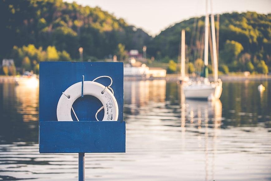 White Lifebuoy on Blue Stand by Lake with Sailboats