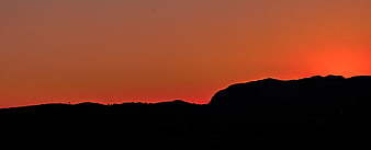 Silhouette of rolling hills against a vibrant orange sunset sky