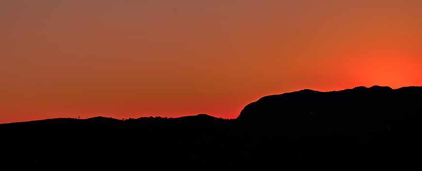 Silhouette of rolling hills against a vibrant orange sunset sky