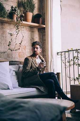 Man with beard sitting on sofa drinking coffee in rustic interior